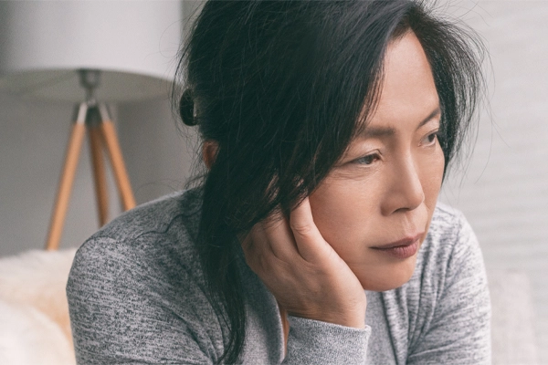 Adrenal-Fatigue-Doctor A middle-aged asian woman sitting on her couch, resting her head on her hand, suffering from adrenal fatigue. Get treatment for adrenal fatigue syndrome from Dr. Lashea Davis Roland in Silver Spring.