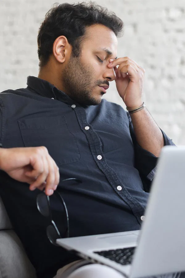 Adrenal-Fatigue-Treatment A middle-aged man with a laptop closing his eyes and rubbing his nose. He needs treatment for Adrenal Fatigue Syndrome from Dr. Lashea Davis Roland in Silver Spring.