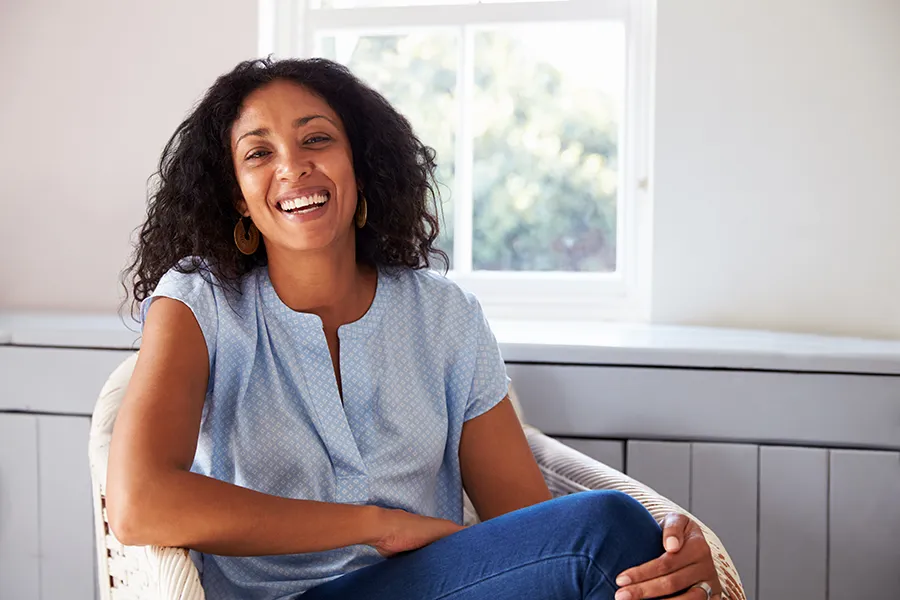 A black woman smiles and relaxes sitting by a window in the sun. Get Anti-Aging treatments from Dr. Lashea Davis Roland in Silver Spring.