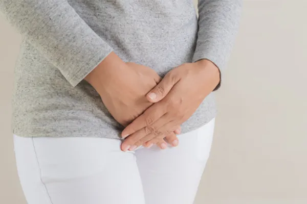 Fibroids-Clinic Close up of a woman in a gray shirt and white pants holding her hands below her abdomen in discomfort. Get treatment for fibroids from Dr. Lashea Davis Roland in Silver Spring.