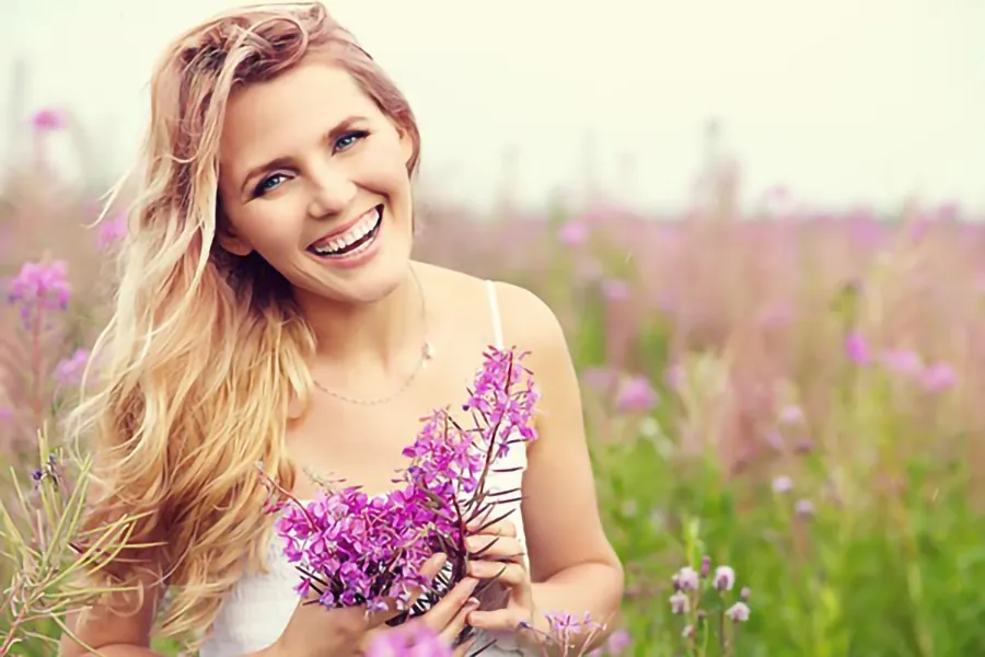 A smiling woman in a field holds a bunch of purple flowers. Get gynecology services from Dr. Lashea Davis Roland in Silver Spring.