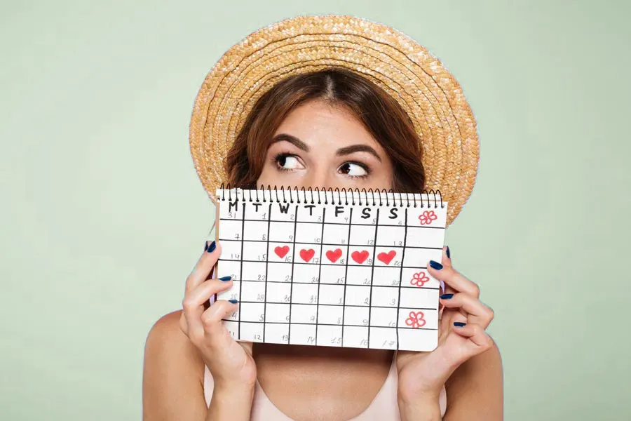 A woman in a straw hat holds a calendar with several days marked off in front of her nose and mouth. Get treatment for menstrual dysfunction from Dr. Lashea Davis Roland in Silver Spring.