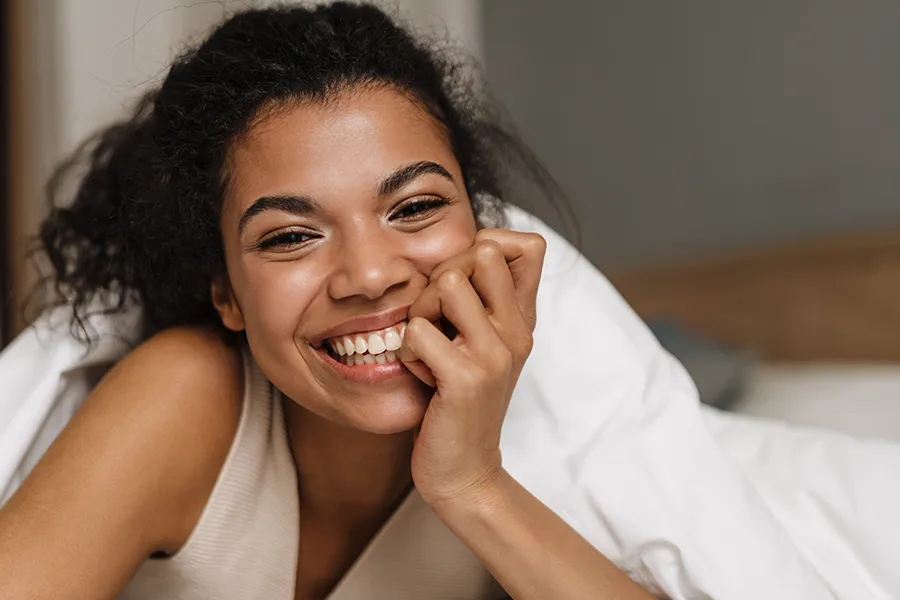 A black woman lying in bed smiling at the camera, excited to have gotten Morpheus8V Vaginal Rejuvenation treatment in Silver Spring by Dr. Lashea Davis Roland.